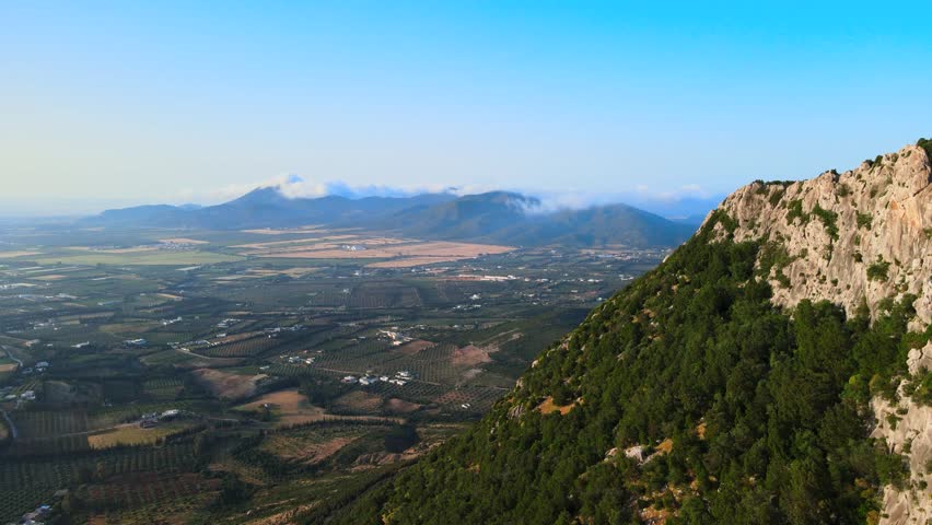 A breathtaking aerial view of Tunisia's Jbal Ressas, showcasing rugged mountains, lush green valleys, and a serene landscape under a clear blue sky.