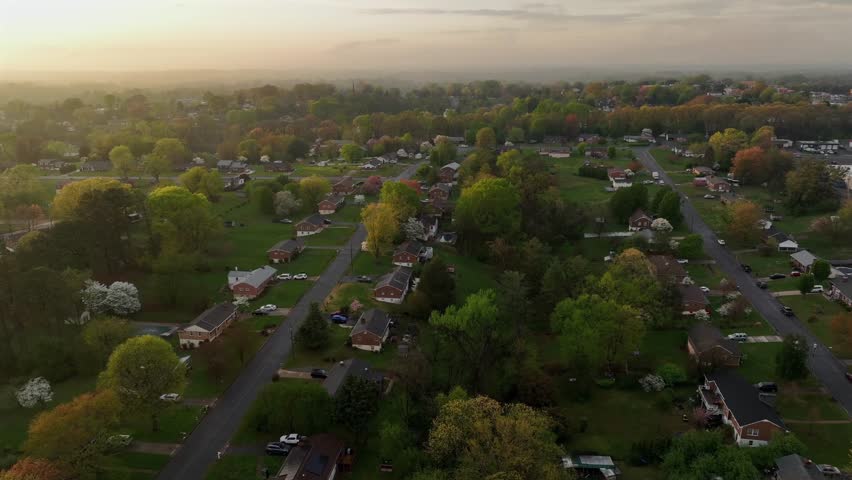Serene landscape atmosphere in idyllic and scenic american neighborhood during sunset. Aerial orbit shot. Red brick one family and two-story houses in green suburb. Foggy and misty day. Virginia, USA.