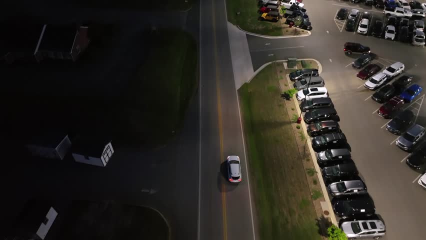 Parking cars on lot of american suburb at night. White car on interstate road during sunset time. Aerial tilt up wide shot. American city in Michigan, USA.