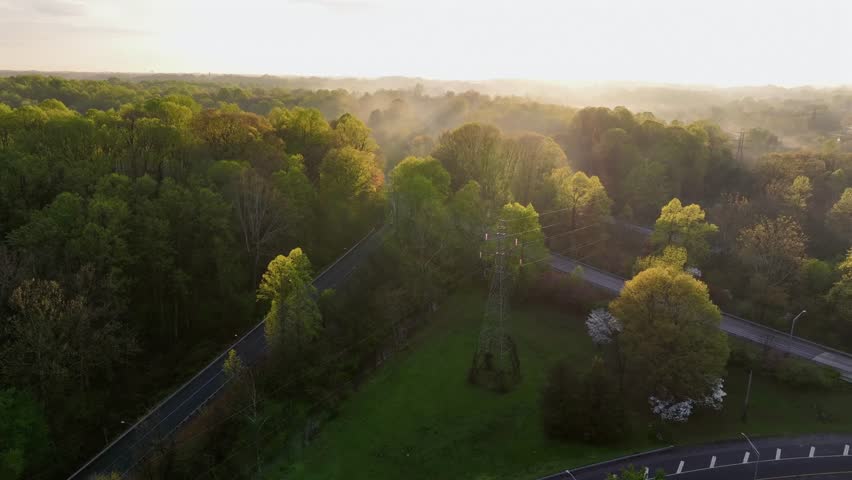 Cars driving on suburb interstate road in American. during golden sunrise. Mystic fog fling between green and yellow colored trees. Aerial establishing wide shot scene in USA.