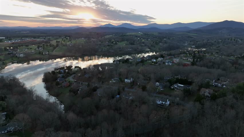 Slow drone flight over quiet and peaceful american suburb neighborhood near James River. Sunset time with reflection on water surface. Beautiful spring day with colored trees and mountain peaks in USA