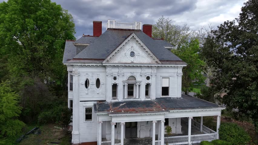 Victorian architecture House, characterized by intricate details, decorative trim and steep gable roof. White facade with large porches and ornate woodwork. Spring day. Aerial view. Virginia, USA.