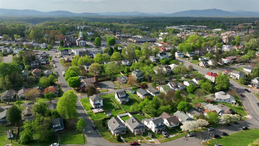 Small american town with two-story one family houses and driving cars on street. Sunny day in spring season and green yards. Historic church in Background. Aerial wide shot. Virginia, USA.
