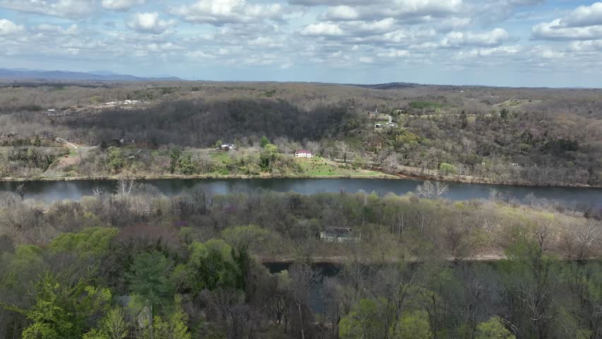 Victorian House with blue roof in idyllic suburb neighborhood. James River in Background. Descend drone wide shot. Blossoming colored trees in spring season. Clouds at sky.