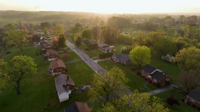 Picturesque golden sunset landscape in american neighborhood.Aerial flyover wide shot. Colored trees during beautiful calm spring evening.Two-story single family house in middle class residential area