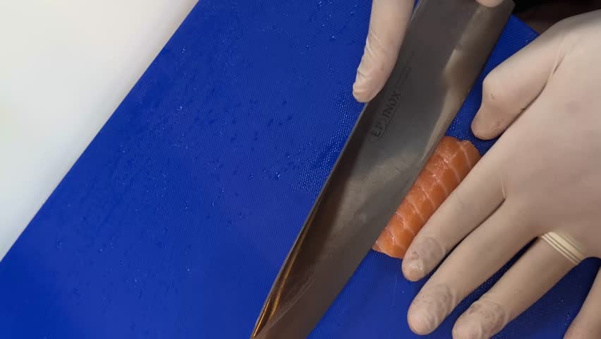 A person in white gloves expertly slices vibrant raw salmon fillet on a blue cutting board specifically intended for fish preparation, highlighting fresh fish use.