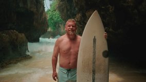 Sporty old man holds a surfboard on tropical island beach. Healthy senior man surfs in Bali, Uluwatu, make surfing. Elderly retired people enjoy outdoor active lifestyle water sport. Adult man surfs. - Powered by Shutterstock - Get 15% off with code: PIKWIZARD15