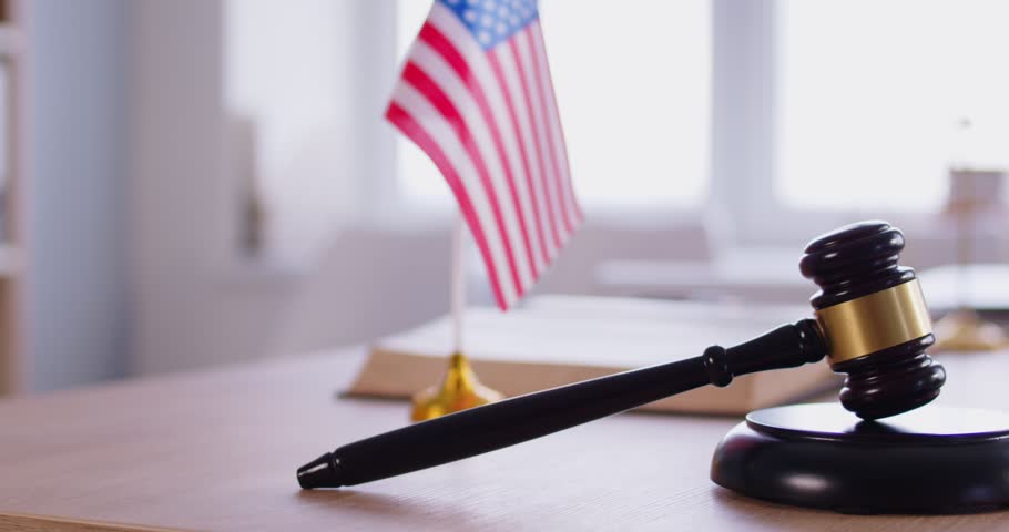 Wooden judge gavel against national USA flag. Justice and law in America. Judges workplace. Constitution, judgement, patriotism and legal system. Judge's hammer for attention and verdict. 