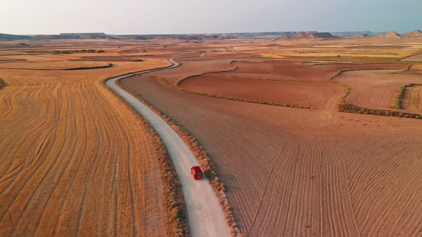 Red car driving through the mountainous desert landscape of Bardenas Reales de Navarra, Spain. An aerial view of the badlands in southeast Navarre
