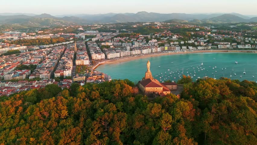 Aerial view of the beautiful coast of San Sebastian at sunset, Basque country, Spain. Flying over the statue of Christ stands watch over magnificent Bay of Biscay, Donostia. Orbit shot