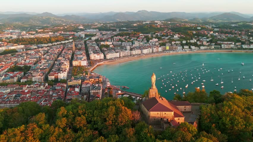 Aerial view of the beautiful coast of San Sebastian at sunset, Basque country, Spain. Flying over the statue of Christ stands watch over magnificent Bay of Biscay, Donostia. Orbit shot