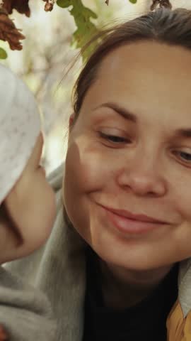 Vertical screen: Girl kissing her mother. Touching moments between parents and daughter in nature in the autumn season at sunset