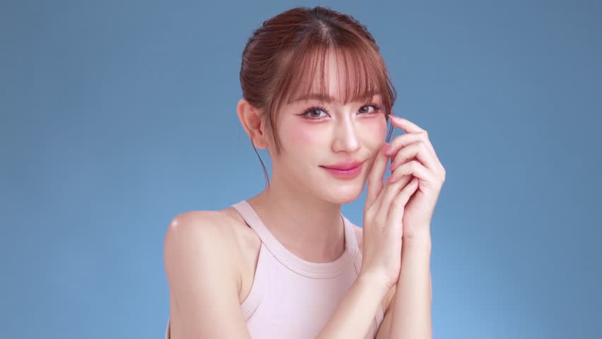 Beautiful young Asian woman model with bangs and natural makeup on face clean fresh skin on isolated blue background. Cute girl portrait, Facial treatment, Body care, Beauty and Spa.