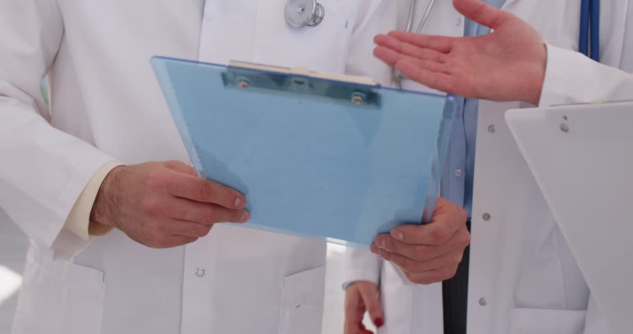 Doctors meet, exchange handshakes, and share research data. Coworkers show each other clipboards, look at test results, read medical reports. Cropped shot, shaking hands closeup. Teamwork concept
