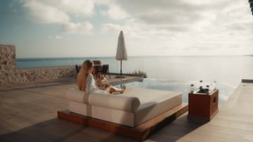 Young Blonde Woman in White Bathrobe Walking to Sunbed to Read a Book with Infinity Pool and Sea View in the background at a Luxury Villa in Greece - Powered by Shutterstock - Get 15% off with code: PIKWIZARD15