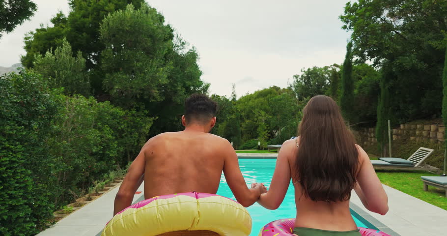 Swimming, couple and jumping in pool with inflatable for travel adventure, recreation and bonding together at resort. Back, people and holding hands with water splash for fun at holiday destination