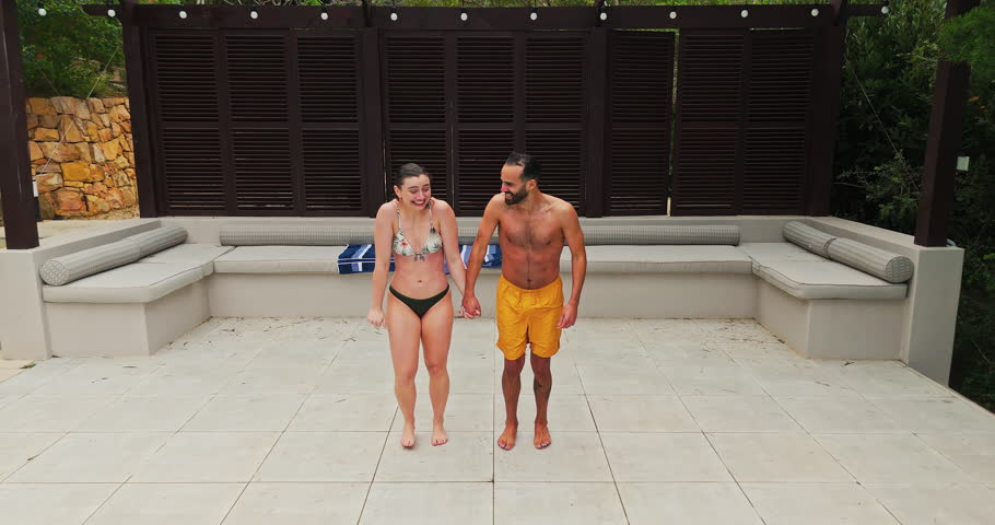 Swimming, couple and jumping in pool with freedom for travel adventure, recreation and bonding together at resort. Energy, people and holding hands with water splash for fun at vacation destination