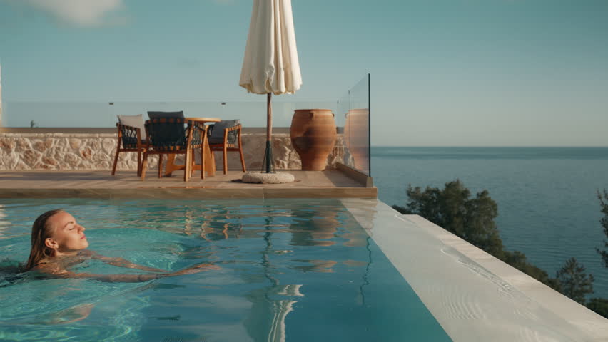 Beautiful Young Woman Swimming to Infinity Pool Edge at Luxury Mediterranean Villa at Summer