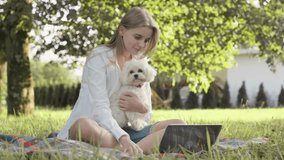 A serene scene of a woman sitting on a blanket in a lush green park, tenderly holding her small dog while engaged with her laptop, blending productivity with the joy of companionship. - Powered by Shutterstock - Get 15% off with code: PIKWIZARD15