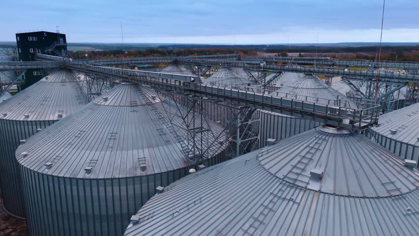 Metal construction connecting large silo tanks at the tops. Drone footage above the stainless steel elevators storing grain.