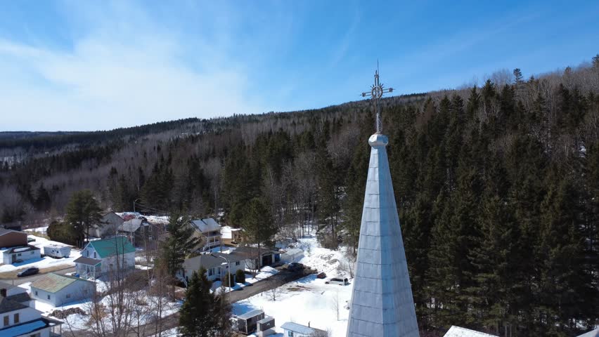 Breathtaking view of the wrought iron cross perched atop a church steeple in a mountain village under a blue sky. Sainte-Florence, Quebec, Canada, 2025.