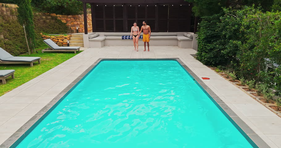 Swimming, couple and jumping in pool on vacation for travel adventure, recreation and bonding together at resort. Freedom, people and holding hands with water splash for fun at holiday destination