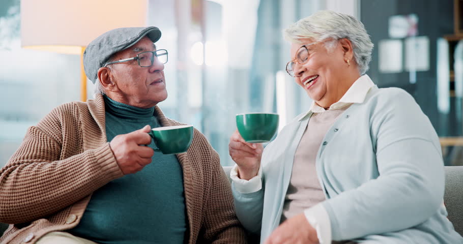 Coffee, laughing and retirement with senior couple on sofa in living room of home together. Bonding, funny or happy with old man and woman drinking caffeine beverage in apartment for relax or romance