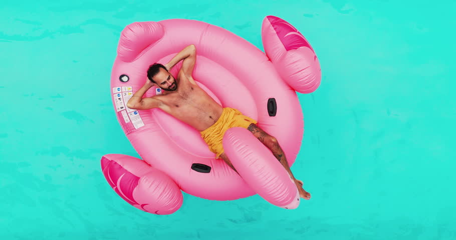 Man, rest and floating in swimming pool outdoor for summer vacation, luxury resort and hospitality trip. Aerial, male person and relax for inflatable flamingo, water and holiday destination at lodge