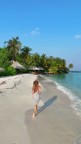 woman runs along the tropical beach at sunset with long shadows cast on the sand, surrounded by calm waves and soft golden light, summer vacation, traveling, family resort, happiness, 