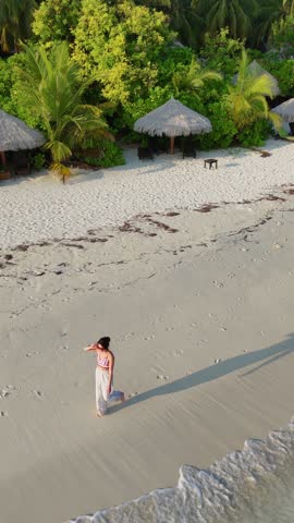 woman runs walks along the tropical beach at sunset with long shadows cast on the sand, surrounded by calm waves and soft golden light, summer vacation, traveling, family resort, happiness, 