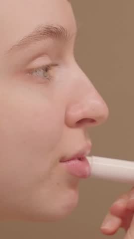 VERTICAL VIDEO: Close-up profile of a beautiful young woman applying hygienic lip balm, nourishing and hydrating her lips for a soft and healthy appearance, enhancing her beauty and self-care routine