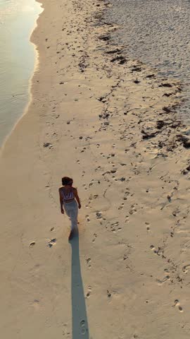 woman runs walks along the tropical beach at sunset with long shadows cast on the sand, surrounded by calm waves and soft golden light, summer vacation, traveling, family resort, happiness, 