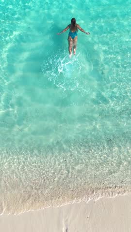 woman runs enters into the tropical beach water at sunset on white sand, surrounded by calm waves and soft golden light, summer vacation, traveling, family resort, happiness