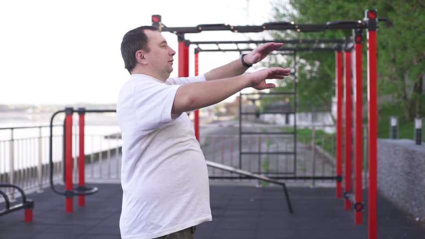 Fat man on the sports ground doing gymnastics to lose weight