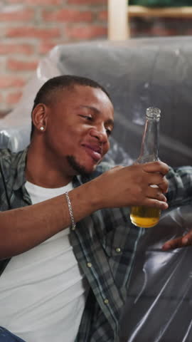 Happy black friends celebrate repair end drinking delicious beer on floor near foiled sofa closeup. African-American workers with alcohol in living room