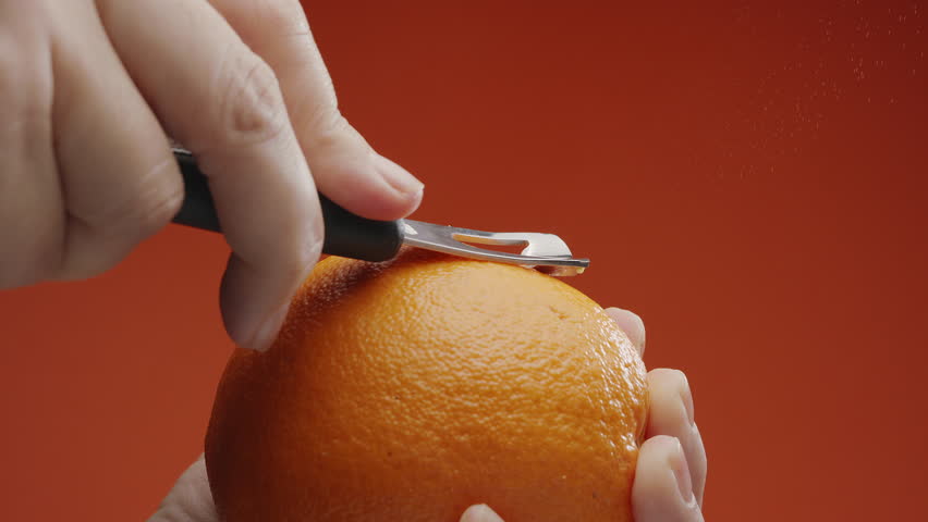 Getting orange peel with a special kitchen tool; orange juice with essential oils sprinkling out under the cut on black background. Slow motion macro video. 