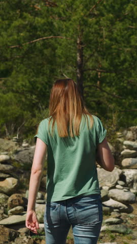 Woman walks between symbolic old stone piles near fir forest backside view slow motion. Place to meditate and rest at highland. Mystical traditions