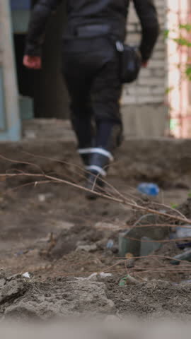 Guy wearing professional moto suit runs into abandoned building doorway backside view slow motion focus on garbage and dry twig in foreground