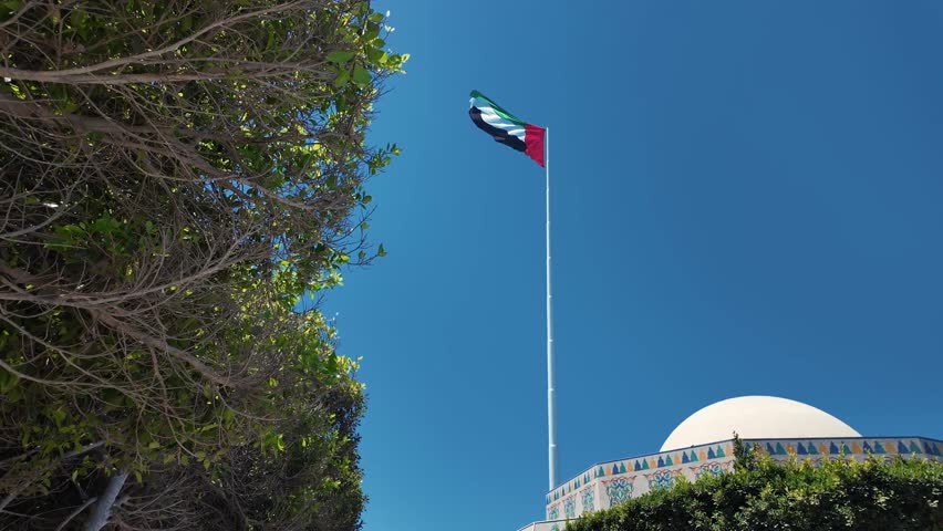 A vibrant view of the UAE flag waving proudly among lush green trees against a bright blue sky