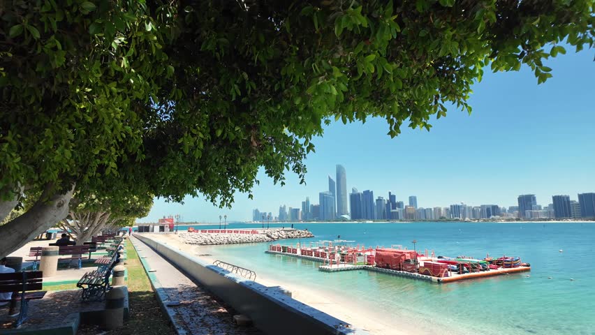 A scenic view of the Abu Dhabi Corniche under the bright sun, showcasing the city skyline and traditional boats.