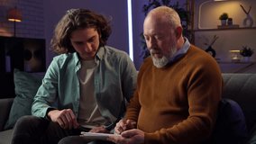 An elderly man learns how to draw on a graphics tablet and a young man controls the process using a laptop. Grandson teaches grandfather how to design while sitting at home in the evening. - Powered by Shutterstock - Get 15% off with code: PIKWIZARD15