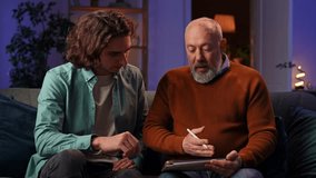An elderly man learns how to draw on a graphics tablet and a young man controls the process using a laptop. Grandson teaches grandfather how to design while sitting at home in the evening. - Powered by Shutterstock - Get 15% off with code: PIKWIZARD15