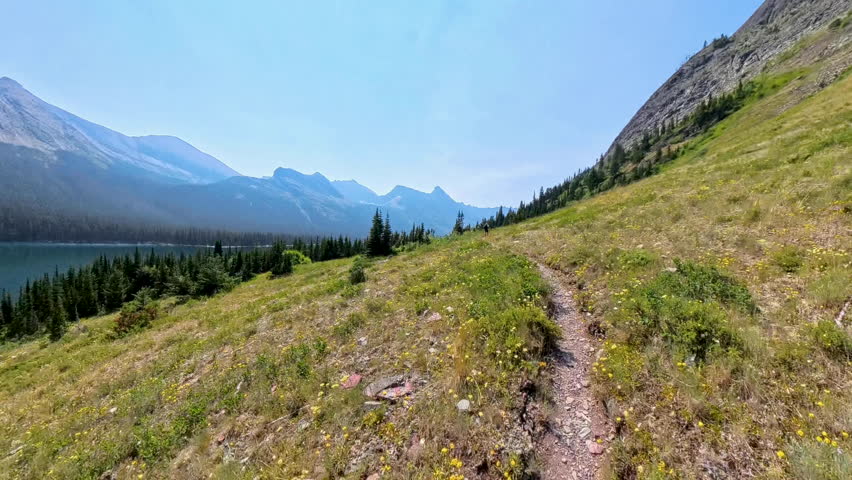 Man Hikes Ahead on Narrow Trail Next to Elizabeth Lake in Glacier National Park