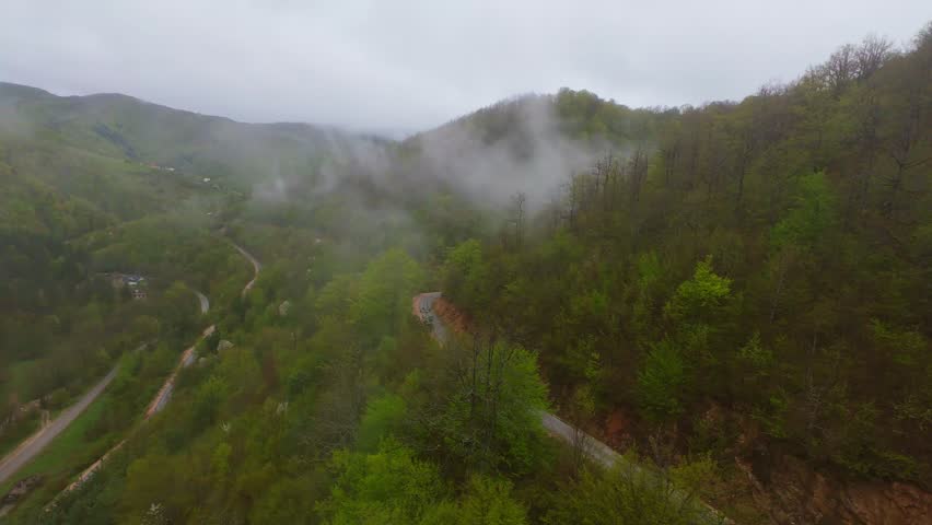 Aerial view of a foggy mountain road weaving through verdant hills, misty forests, and scenic valleys, offering a breathtaking natural backdrop for travel, tourism, adventure, and countryside drives