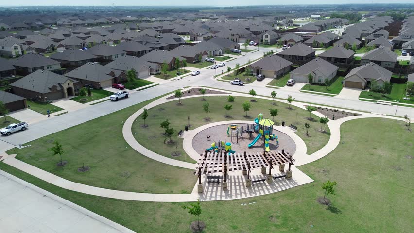 Modern circular children playground with climbing structures, slides, spring riders, wooden pergola in Princeton, growing small town in Dallas Metroplex, Collin County in North Texas, flyover. USA
