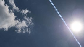 Bright sunlight creating dramatic lens flare near airplane contrail stretching across pristine blue sky with scattered white clouds - Powered by Shutterstock - Get 15% off with code: PIKWIZARD15