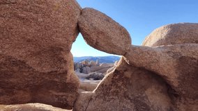 Landscape view of Arch Rock or Joshua Tree National Park in California. Distant mountains and sky visible through an arch. - Powered by Shutterstock - Get 15% off with code: PIKWIZARD15