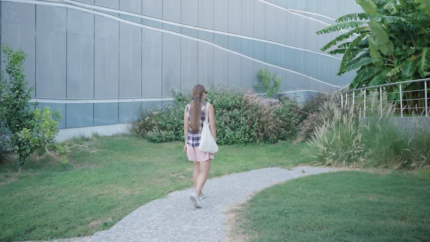 Woman Ascends Stone Steps with a White Bag, Passing Tall Green Plants in a Park Area.