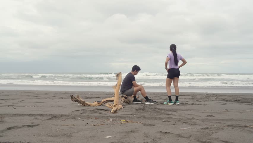 active young asian couple resting and chatting after running exercise on the beach