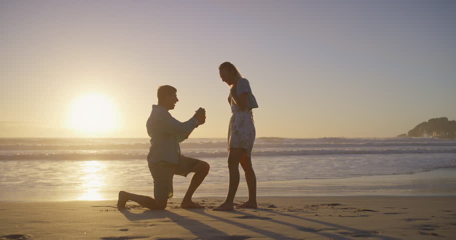 Celebration, hug and proposal with couple on beach together for commitment, love or marriage. Engagement, happiness or sunset with happy man and woman on sand by ocean or sea to ask the question